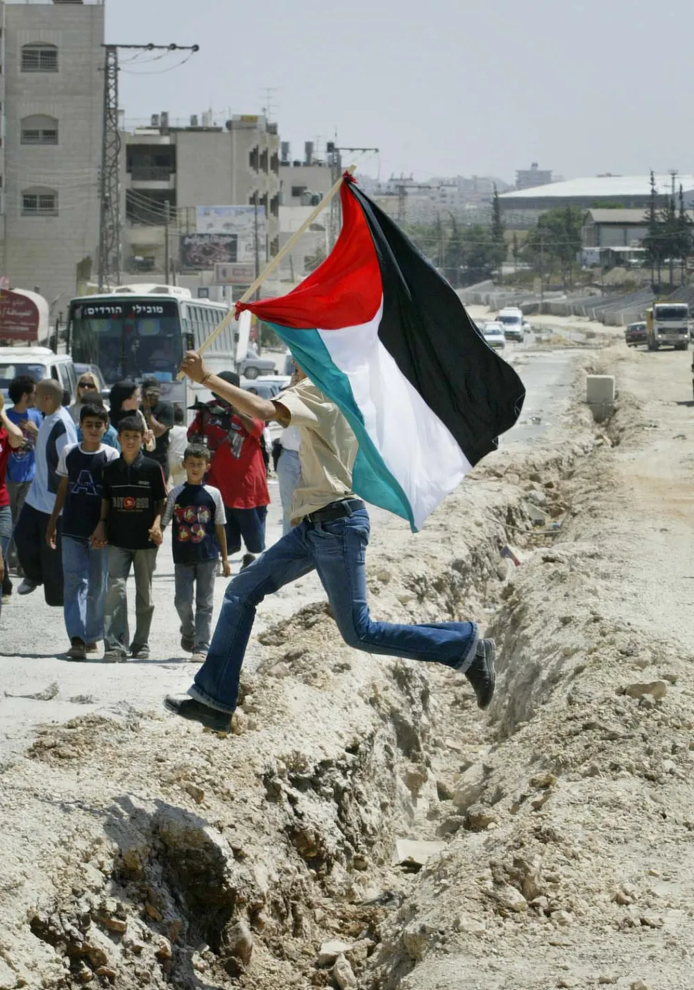 A Palestinian demonstrator jumps over a ditch to be used as foundation for the construction of Israel's separation barrier, during a demonstration against the barrier, in A-ram in the outskirts of Jerusalem, Friday July 23, 2004. (AP Photo/Oded Balilty)