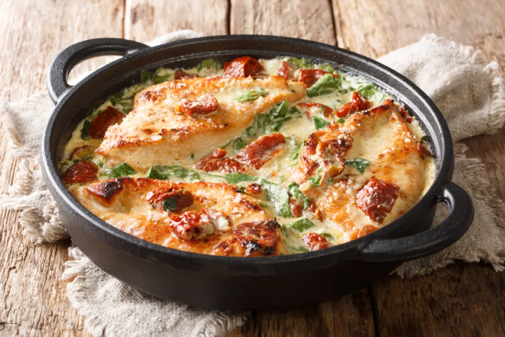 Main course baked chicken with sun-dried tomatoes and spinach in cheese sauce close-up in a pan on the table. horizontal