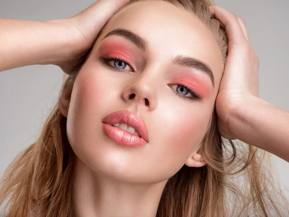 Portrait of a beautiful woman with a coral color makeup. Attractive blonde girl with bright fashion make-up, posing at studio. Beautiful female face. Closeup portrait of pretty lady. Fashion model.