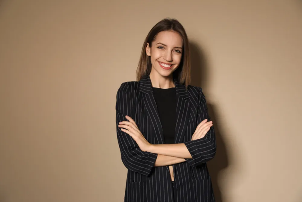 Portrait of beautiful young woman in fashionable suit on beige background. Business attire