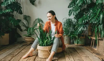 A beautiful young woman is sitting on the floor in her green garden or greenhouse, taking care of plants. The concept of gardening, landscaping in urban conditions