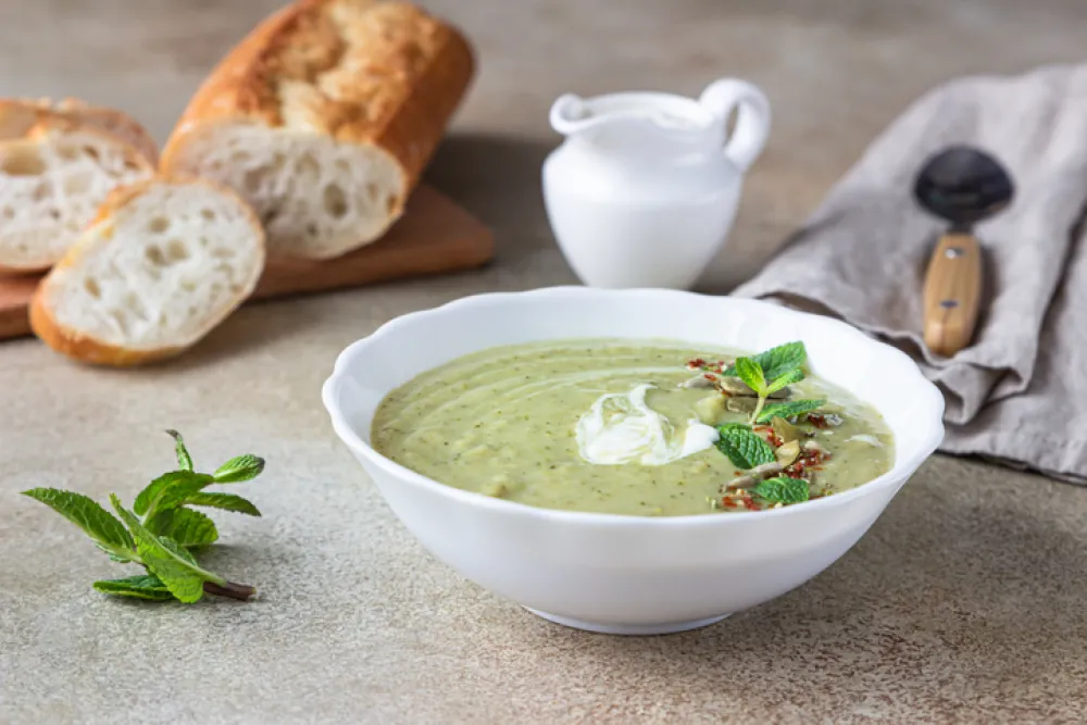 Broccoli cream soup served with mint, cream, seeds and fresh bread on concrete background. Healthy vegetarian food concept. Selective focus.