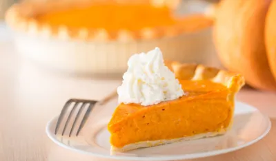 Pumpkin pie with swirls of whipped cream on decorative plate. Whole pie in soft focus in background. Macro with shallow dof