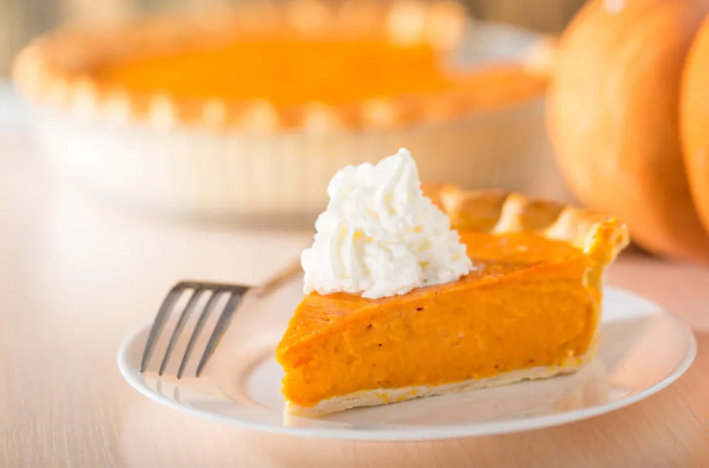 Pumpkin pie with swirls of whipped cream on decorative plate. Whole pie in soft focus in background. Macro with shallow dof