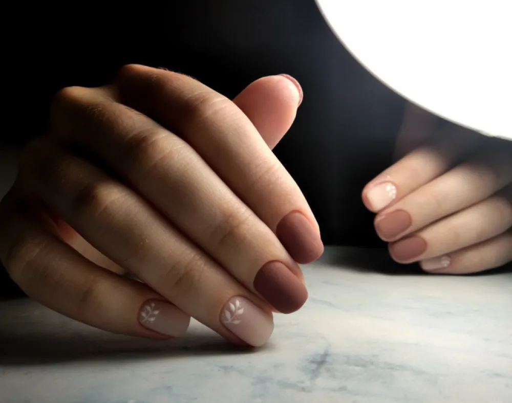Gentle coffee manicure with white design. Short square nails with brown-beige coating and the design of twigs.