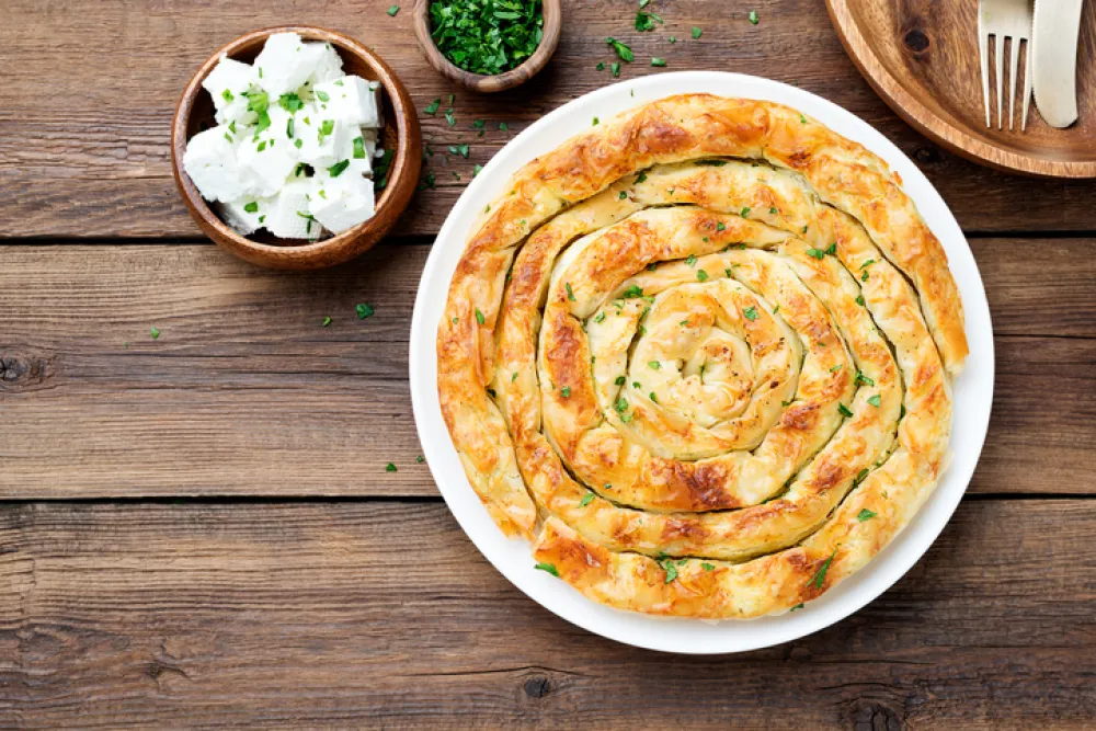 Traditional feta cheese phyllo pastry pie on wooden background.
