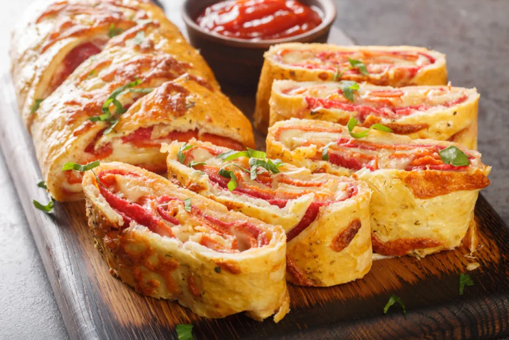Italian food Pizza roll stromboli with cheese, salami and tomatoes closeup on the wooden board on the table. Horizontal<br>