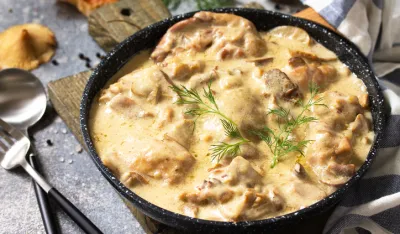 Fricasse - French Cuisine. Chicken stewed in a creamy sauce with mushrooms in a pan on a light stone background.