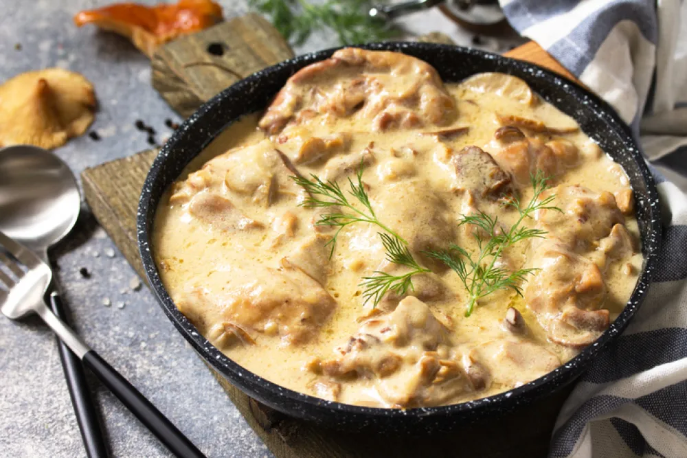 Fricasse - French Cuisine. Chicken stewed in a creamy sauce with mushrooms in a pan on a light stone background.