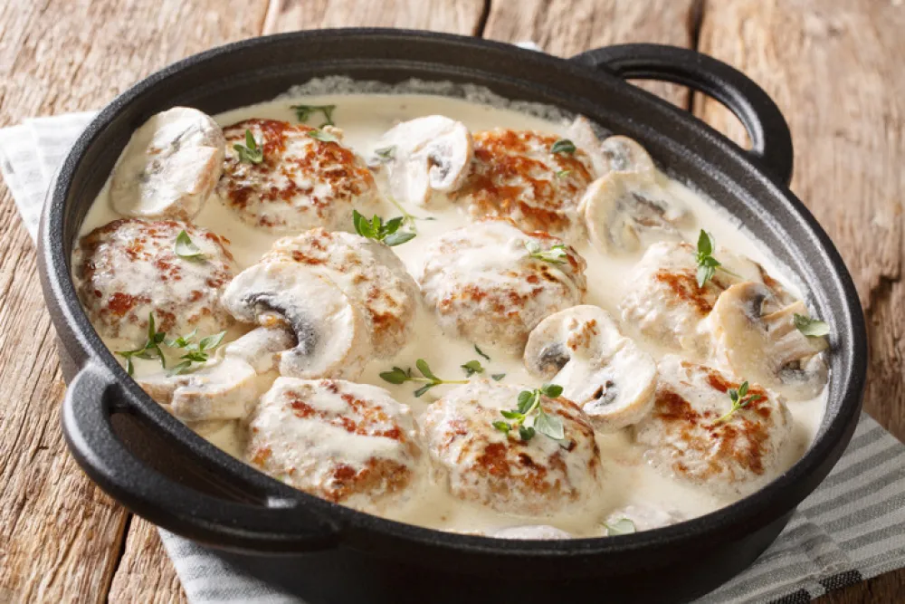 Homemade meatballs cooked with mushrooms served in a creamy sauce with thyme closeup in a pan on the table. horizontal<br>