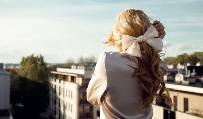Pretty girl in romantic outfit with wonderful hairstyle and big elegant bow standing back and looking around from observation platform closeup. Trend look, relaxation on roof, sky, paris cityscape. 