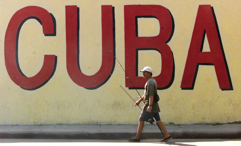 HAV02D:CUBA:HAVANA,4JUL00 - A Cuban fisherman walks in front of a mural in central Havana July 4. Cuban government officials criticized American immigration policies that they blame for the Elian Gonzalez case, saying that the law allowing Cubans to remain in the U.S. on reaching American soil encourages people to make dangerous journeys across the sea. kw/Photo by Kimberly White REUTERS