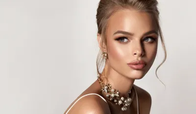 Portrait of perfectly looking woman dressed in splendid evening makeup. Ripe lips, painted in rose color, long black eyelashes and side glance of beautiful eyes. Elegant jewellery set of earrings and necklace on her. Beauty, hairstyling and cosmetic.