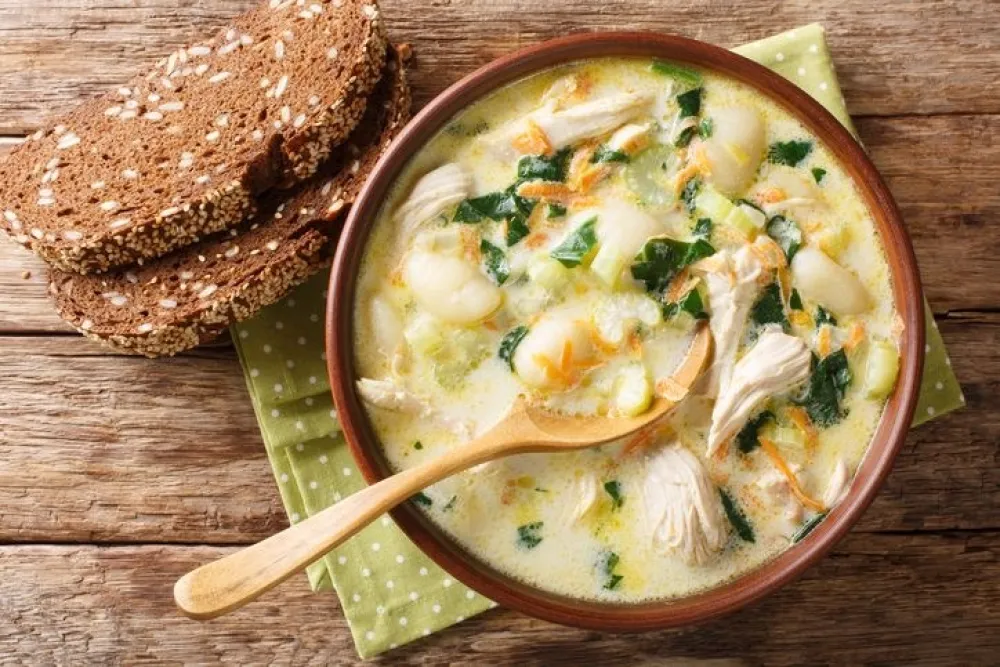 cream soup with gnocchi, chicken and spinach served with bread close-up in a bowl on the table. Horizontal top view from above<br>